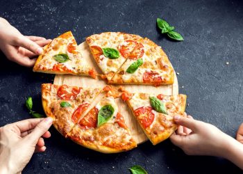 tavolo nero una pizza margherita tagliata a fette con mani che prendono fette
