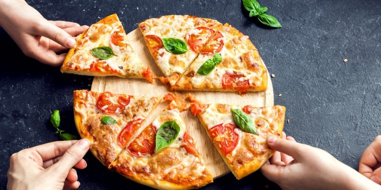 tavolo nero una pizza margherita tagliata a fette con mani che prendono fette