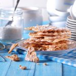 Dolci di carnevale: su tavola azzurra un piatto con le chiacchiere al forno e un vasetto di zucchero accanto