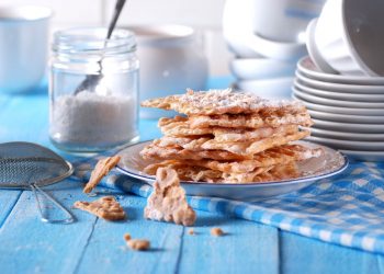 Dolci di carnevale: su tavola azzurra un piatto con le chiacchiere al forno e un vasetto di zucchero accanto