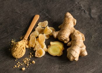 dei pezzi di radice di zenzero con accanto un cucchiaio di legno colmo di polvere di zenzero