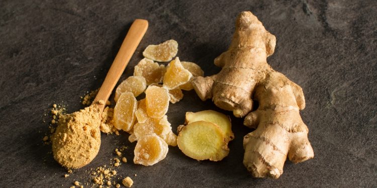 dei pezzi di radice di zenzero con accanto un cucchiaio di legno colmo di polvere di zenzero
