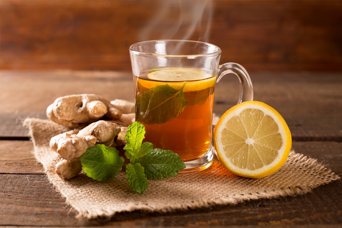 una tazza in vetro con una tisana di zenzero e limone con accanto un pezzo di radice di zenzero e mezzo limone