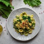 Cime di rapa e pasta: un primo veloce con le verdure 1 su tavolo di marmo bianco: piatto grigio con le orecchiette con cime di rapa, olio EVO e in fono broccatelli su tagliere