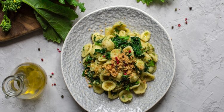 su tavolo di marmo bianco: piatto grigio con le orecchiette con cime di rapa, olio EVO e in fono broccatelli su tagliere