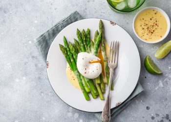 ricette con asparagi: su base grigio chiaro piatto tondo con uovo su letto di asparagi