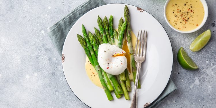 ricette con asparagi: su base grigio chiaro piatto tondo con uovo su letto di asparagi
