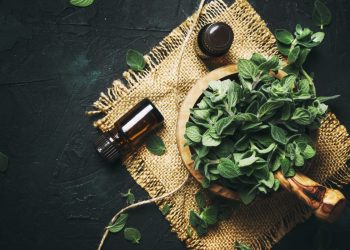su fondo scuro, tovaglietta con ciotola con foglie di origano fresco e flaconcini sparsi