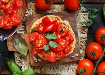 ricette con pomodori: su piatto di legno una frisella con pomodorini e foglie di basilico