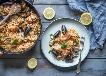 su base di legno celeste padella e piatto con risotto alla pescatora
