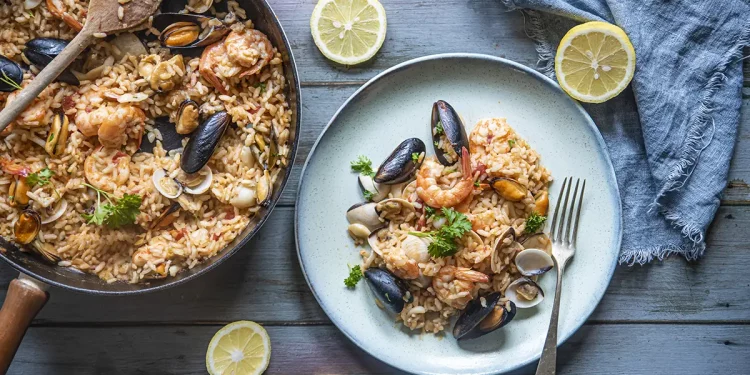 su base di legno celeste padella e piatto con risotto alla pescatora