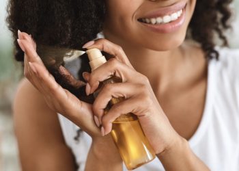Una giovane donna che spruzza sui capelli un olio ristrutturante