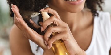 Una giovane donna che spruzza sui capelli un olio ristrutturante