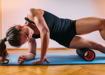 donna con tappetino che esegue con il foam roller un esercizio per allentare la tensione alle gambe