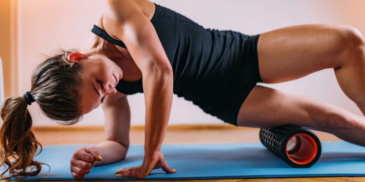 donna con tappetino che esegue con il foam roller un esercizio per allentare la tensione alle gambe