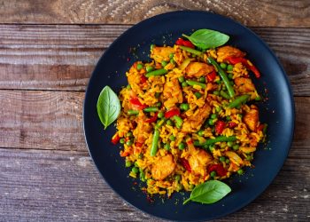 su un tavolo di legno: una paellera con paella di pollo con fagiolini e piselli