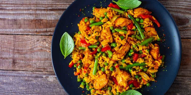 su un tavolo di legno: una paellera con paella di pollo con fagiolini e piselli
