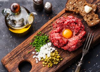 su tavolo di marmo nero, tagliere con una tartare di manzo e prezzemolo, cipolle e capperi tritati con una bottiglia di olio Evo