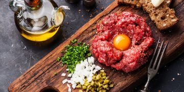 su tavolo di marmo nero, tagliere con una tartare di manzo e prezzemolo, cipolle e capperi tritati con una bottiglia di olio Evo