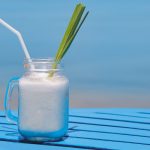 con sfondo di mare, tavolo azzurro con bicchiere con manico con un virgin colada, foglia di ananas e cannuccia