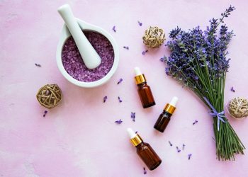 su base lilla un mortaio bianco con foglie di lavanda, un mazzetto di lavanda e 3 flaconcini