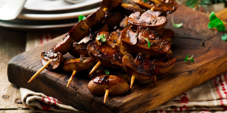 vassoio di legno con spiedini di funghi arrosto