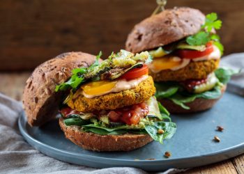 su tavolo di legno canovaccio sotto un piatto azzurro con un hamburger vegetariano fatto con patate e lenticchie