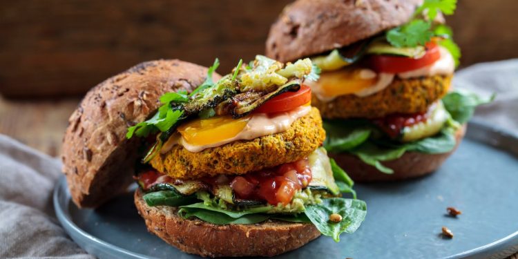 su tavolo di legno canovaccio sotto un piatto azzurro con un hamburger vegetariano fatto con patate e lenticchie