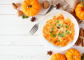 scodella bianca con pasta lunga alla zucca, zucche sparse intorno