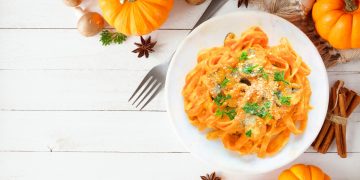 scodella bianca con pasta lunga alla zucca, zucche sparse intorno