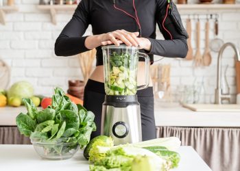 le mani di una donna sul frullatore pieno di verdure