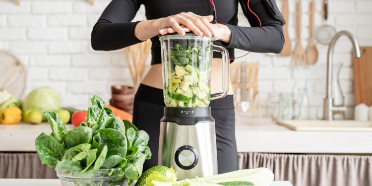 le mani di una donna sul frullatore pieno di verdure