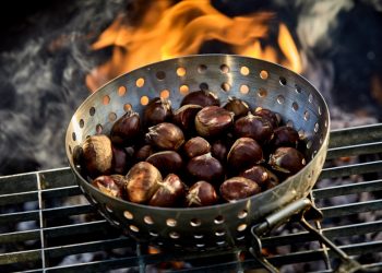 padella di ferro bucata piena di castagne su griglia e sul fuoco
