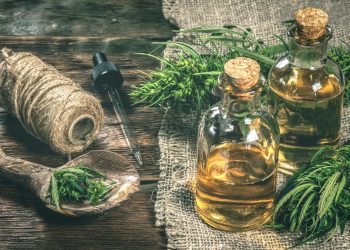 due boccette di vetro con olio di canapa, foglie della pianta di canapa e un rotolo di filo di canapa