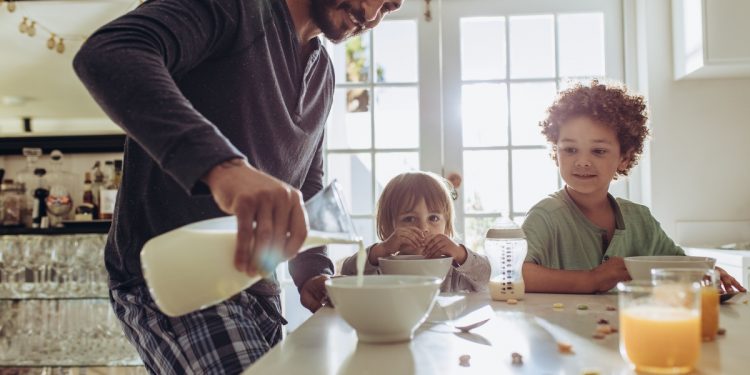 un papà che versa del latte ai due figli per colazione