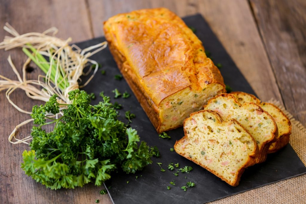 Plumcake salato: ricetta base e idee per farcirlo 2 su tavolo di legno, tagliere nero con plumcake salato al salmone e un mazzo di prezzemolo