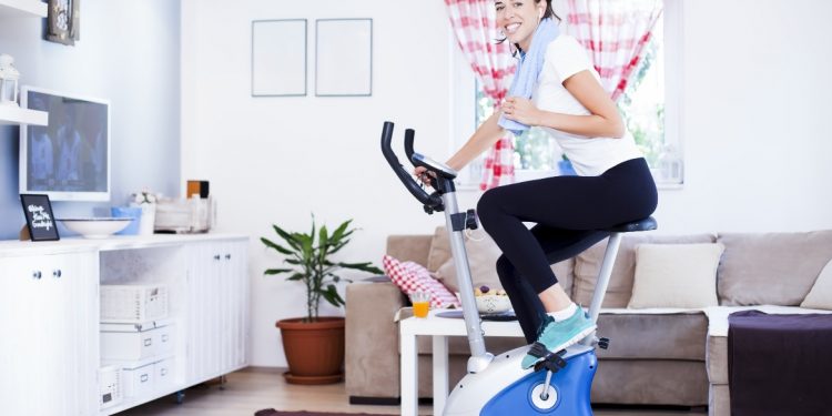 una donna nel salotto di casa sua che si allena con la cyclette