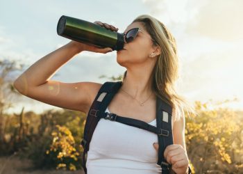 donna in montagna che fa trekking e beve acqua dentro una borraccia termica