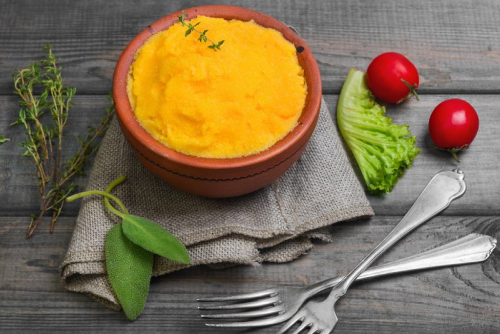 su base di legno ciotola di coccio con polenta con carote e verza