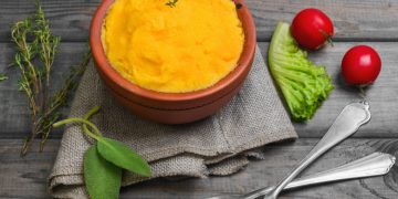 su base di legno ciotola di coccio con polenta con carote e verza