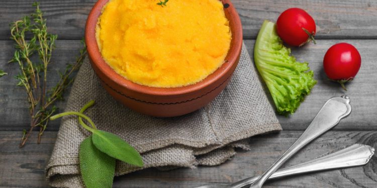 su base di legno ciotola di coccio con polenta con carote e verza