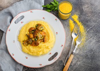 piatto tondo decorato e al centro una ricetta con la polenta con funghi, posate e tovagliolo intorno