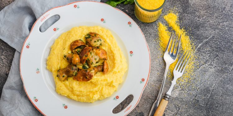 piatto tondo decorato e al centro una ricetta con la polenta con funghi, posate e tovagliolo intorno