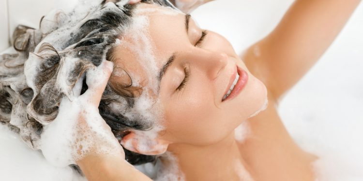 donna in vasca da bagno che si lava i capelli con uno shampoo all'acido ialuronico