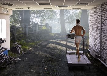 Uomo nel garage di casa sua ha creato una palestra in casa e corre sul tapis roulant sulla destra piccoli attrezzi per tonificarsi