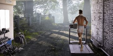 Uomo nel garage di casa sua ha creato una palestra in casa e corre sul tapis roulant sulla destra piccoli attrezzi per tonificarsi