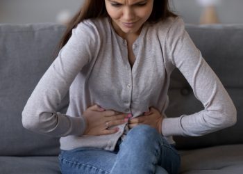 Una donna seduta sul divano piegata in due per il dolore causato dalla pancreatite