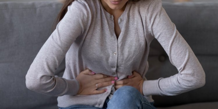 Una donna seduta sul divano piegata in due per il dolore causato dalla pancreatite