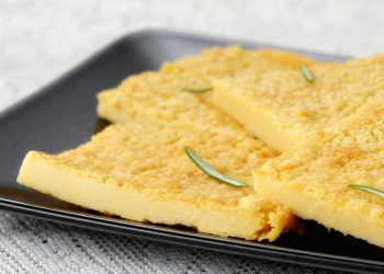 Primo piano su tavolo da cucina con un piatto rettangolare con la farinata di ceci e rosmarino