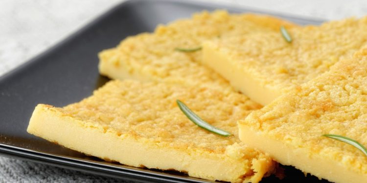 Primo piano su tavolo da cucina con un piatto rettangolare con la farinata di ceci e rosmarino